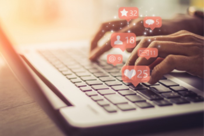 Mãos digitando em um notebook com notificações de redes sociais